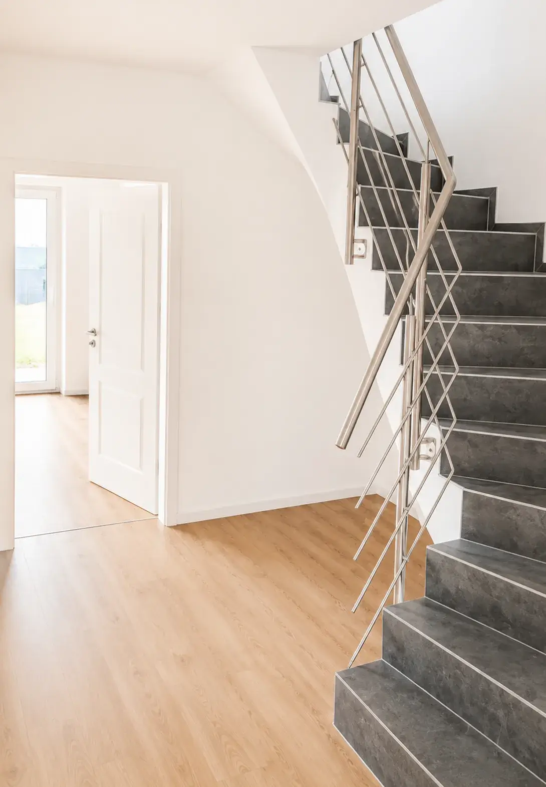 Helles modernes Treppenhaus mit dunklen Stufen, Metallgeländer und Holzboden